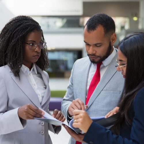 Serious coworkers discussing papers. Focused multiethnic young business colleagues standing together and looking at folder with documents. Business concept